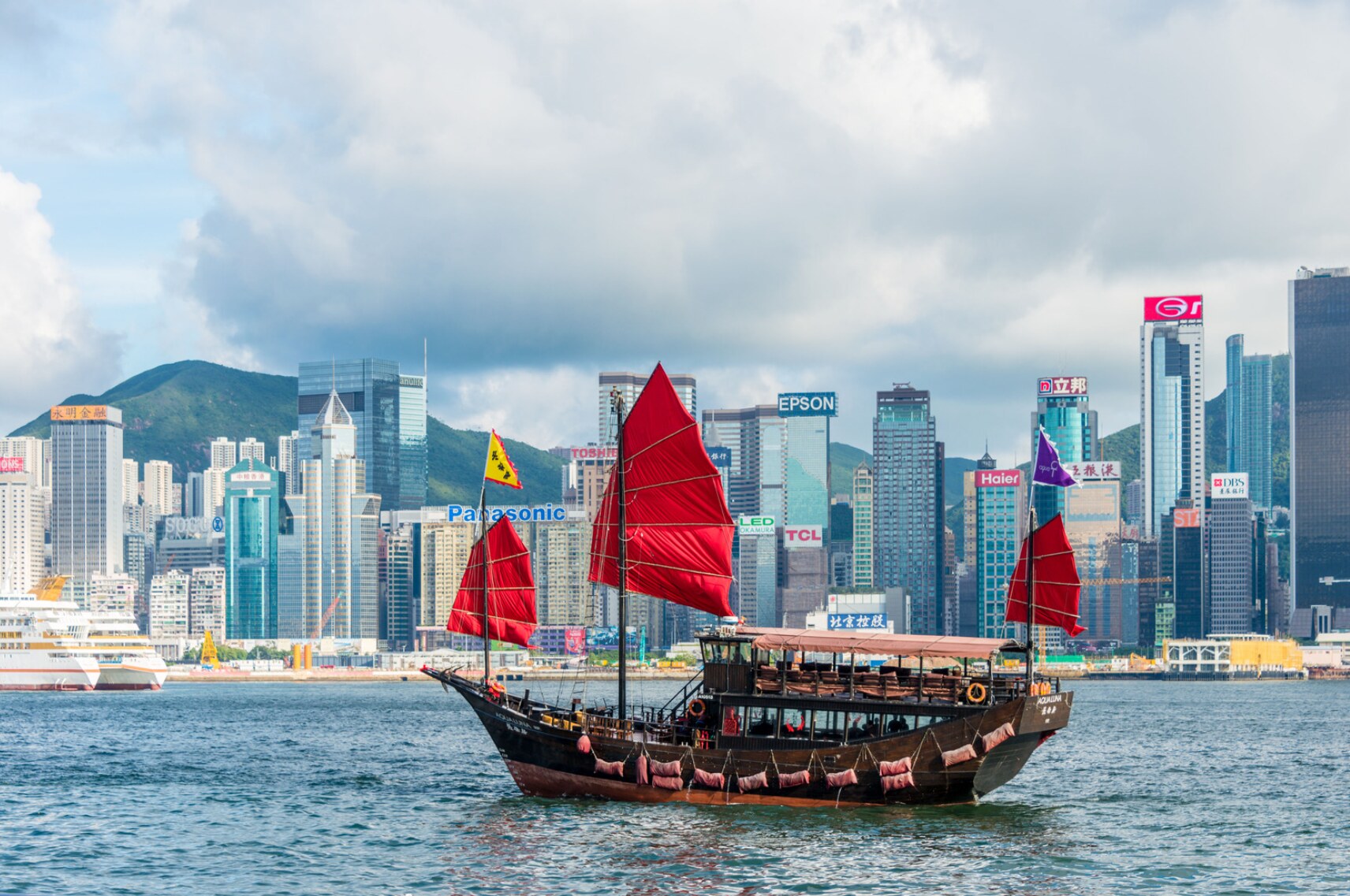 A traditional red-sailed junk boat crossing Victoria Harbour before Hong Kong’s skyline