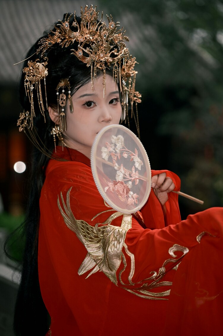 A young woman in ornate traditional Chinese dress holding a round fan