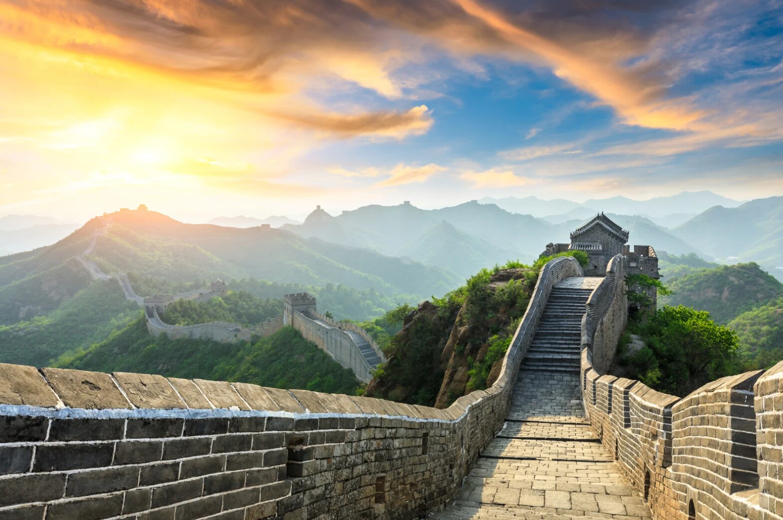 The Great Wall winding over green mountains beneath a dramatic sunrise