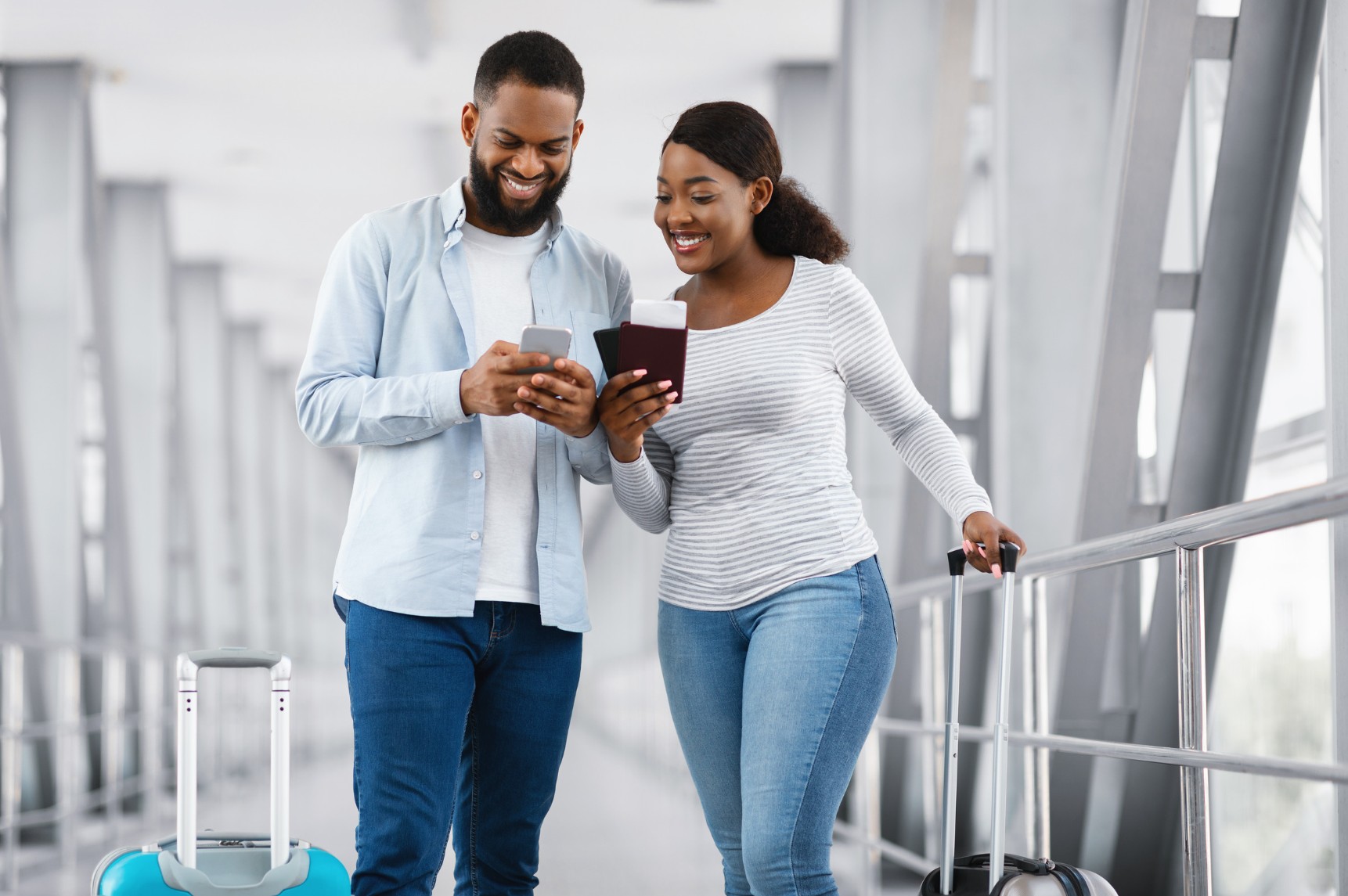 Two travelers with luggage smiling as they check a smartphone and travel documents