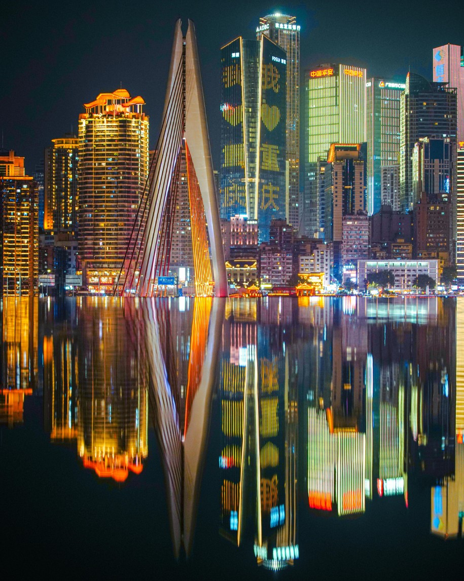 An illuminated city skyline and bridge reflected in a river at night