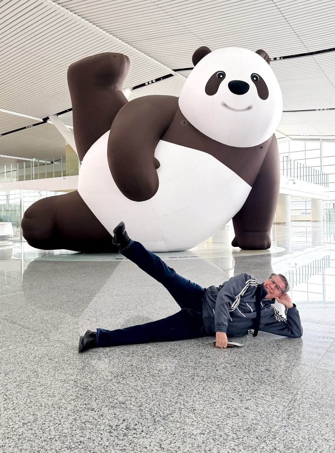 Steve playfully posing on the floor beside a giant panda sculpture in China